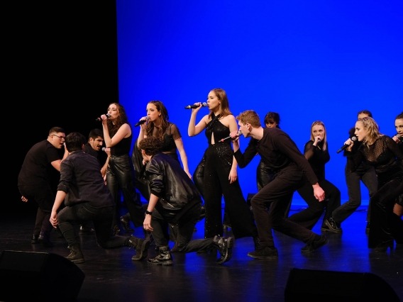 students wearing black singing on a stage with a bright blue backdrop