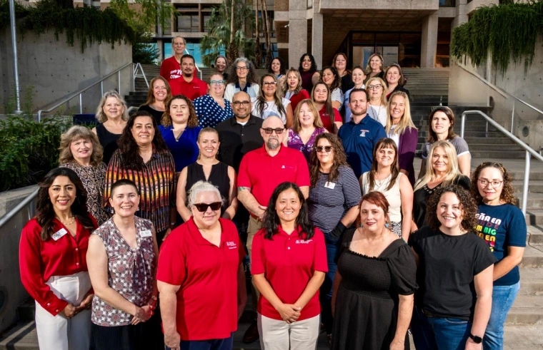 Group photo of several people standing together on the steps outside the University of Arizona main library, smiling at the camera.